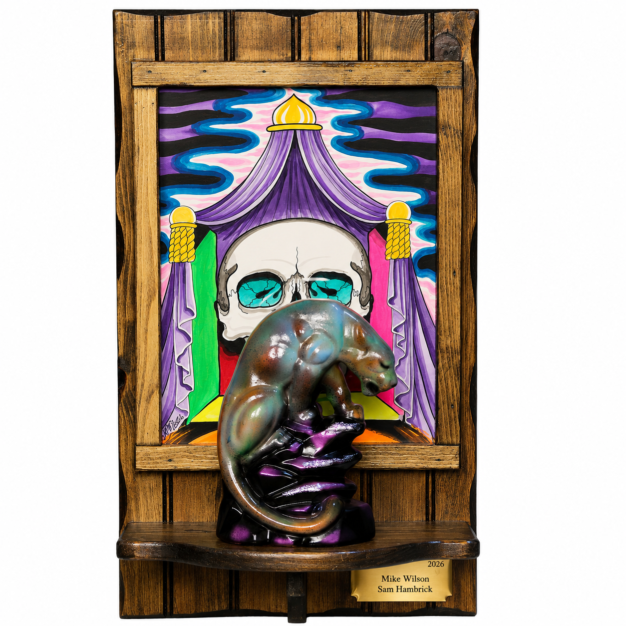 A framed art piece featuring a colorful painting of a skull under purple drapery, with a sculptural rat figurine in the foreground and a small plaque at the bottom reading Mike Wilson and Sam Hambrick.