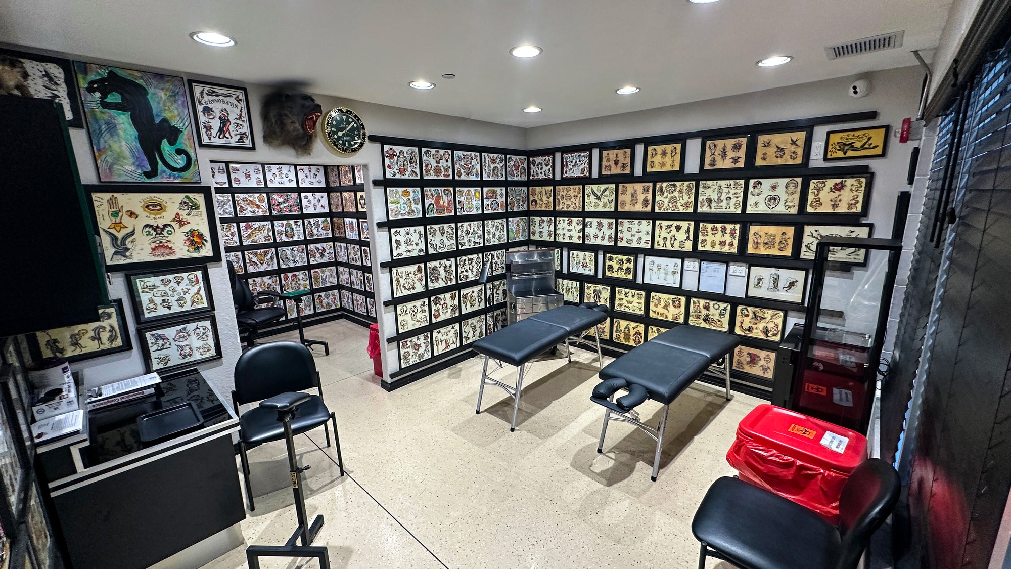 Tattoo studio interior with tattoo designs on walls, chairs, and equipment.