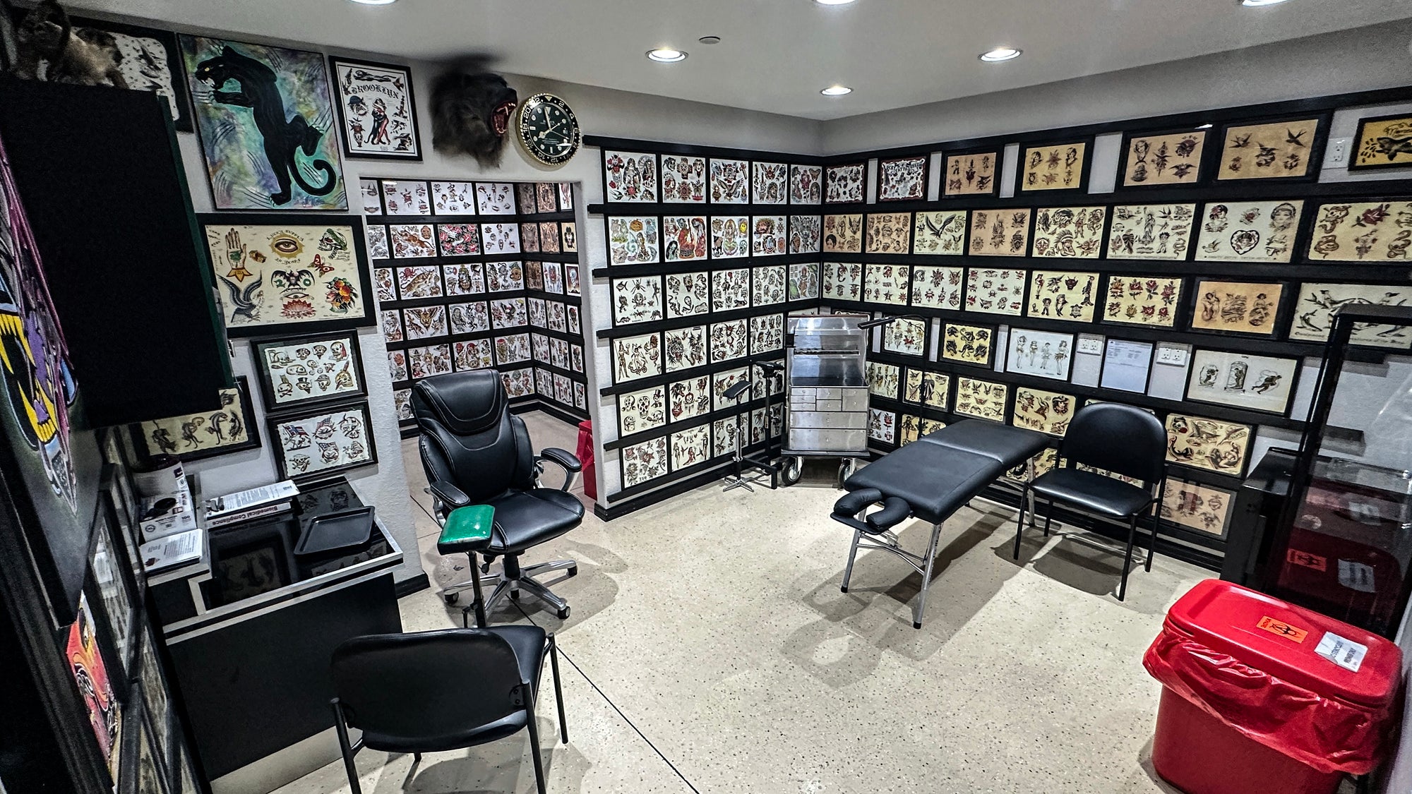 Tattoo studio with various tattoo designs on the walls, chairs, and a table.